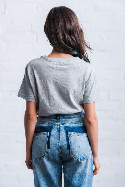 rear view of young woman in empty grey t-shirt in front of brick wall  - Foto, afbeelding