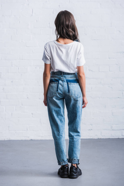 rear view of young woman in empty white t-shirt in front of brick wall  - Fotografie, Obrázek