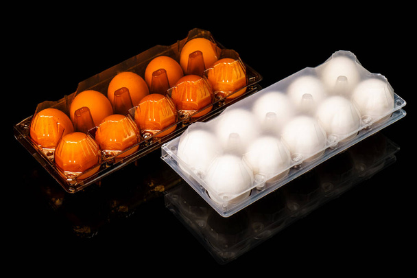 Tuoreet ruskeat ja valkoiset munat läpinäkyvillä muovitarjottimilla mustalla pohjalla
 - Valokuva, kuva