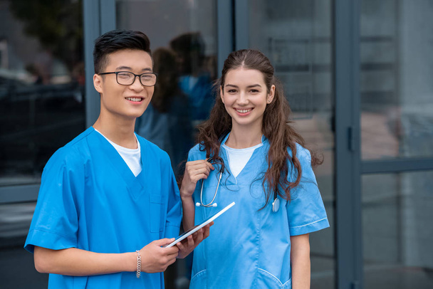 Multikulturelle Medizinstudenten halten Tablet in der Hand und blicken in die Kamera der Medizinischen Universität - Foto, Bild