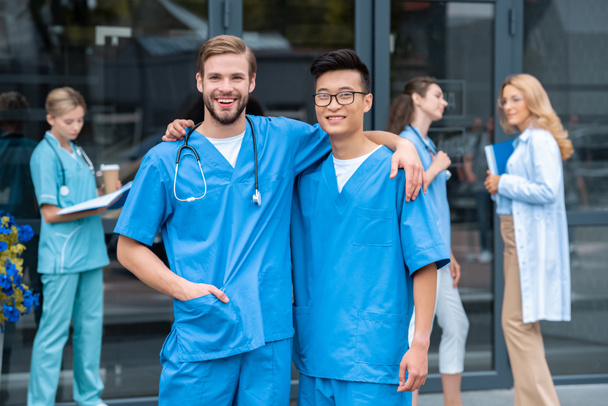 Multikulturelle Studenten umarmen sich und blicken in die Kamera in der Nähe der medizinischen Universität - Foto, Bild