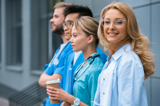 Lächelnder Lehrer mit multikulturellen Studenten, die in der Nähe der medizinischen Universität in einer Reihe stehen  - Foto, Bild