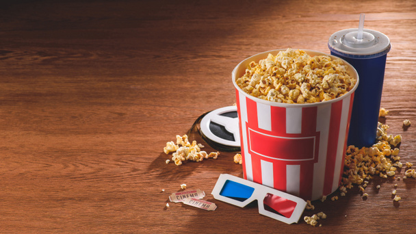 close up view of paper bucket with popcorn, soda drink, 3d glasses on wooden tabletop - Foto, imagen