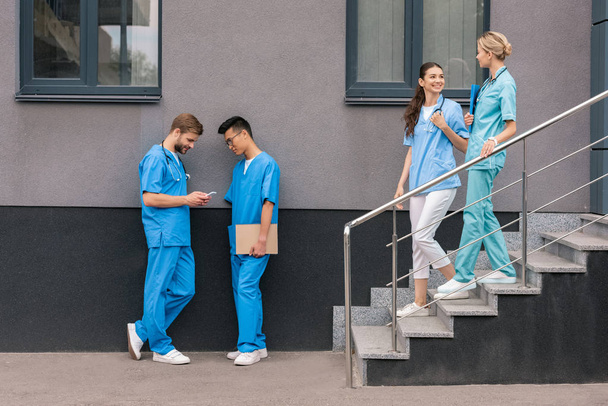πολυπολιτισμική αρσενικό φοιτητές της ιατρικής βλέπουν το smartphone κοντά στο Ιατρικό Πανεπιστήμιο - Φωτογραφία, εικόνα