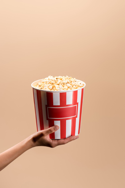 partial view of woman holding disposable bucket with popcorn isolated on beige - Φωτογραφία, εικόνα