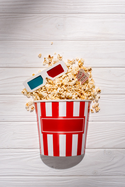 flat lay with disposable bucket with popcorn, retro cinema tickets and 3d glasses on white wooden surface - Foto, Bild