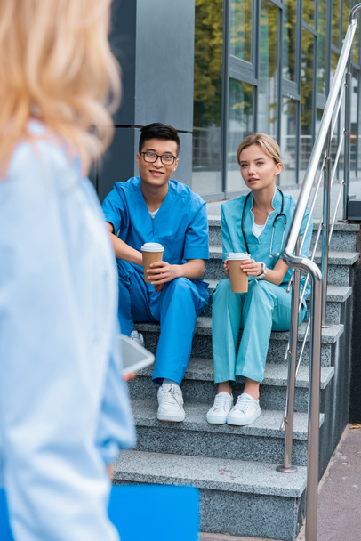 przycięty obraz nauczyciela ogląda studentów medycyny siedząc na schodach z kawy, aby przejść  - Zdjęcie, obraz