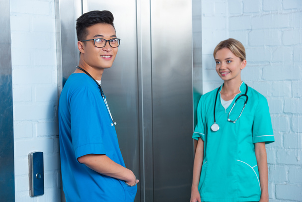 улыбающиеся мультикультурные студенты-медики ждут лифта в университете
 - Фото, изображение