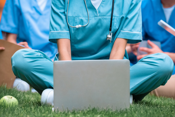 обрезанное изображение студента-медика, занимающегося с ноутбуком на зеленой траве
 - Фото, изображение
