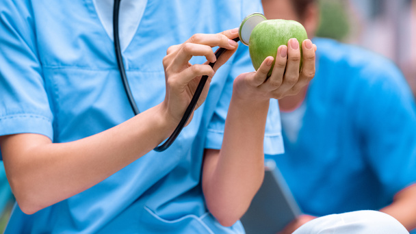 обрезанное изображение студента-медика, изучающего яблоко со стетоскопом
 - Фото, изображение