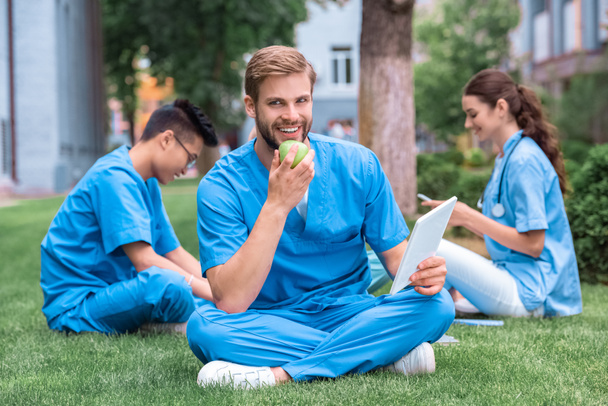 handsome caucasian medical student eating apple and holding tablet - Photo, Image