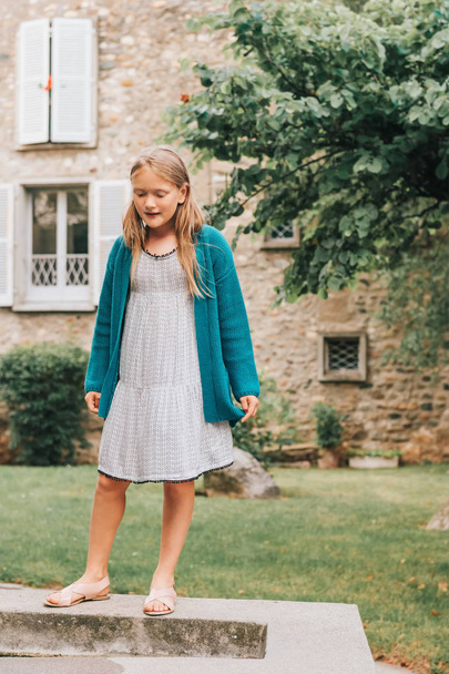 На відкритому повітрі портрет чарівної маленької дівчинки, яка грає в красивому саду, в літній сукні, сандалі і зелений кардиган
 - Фото, зображення
