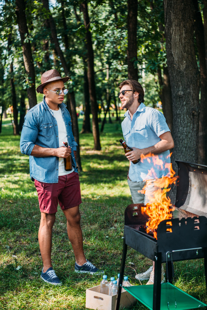 multiethnic friends with beer having conversation near grill in park - Foto, Bild