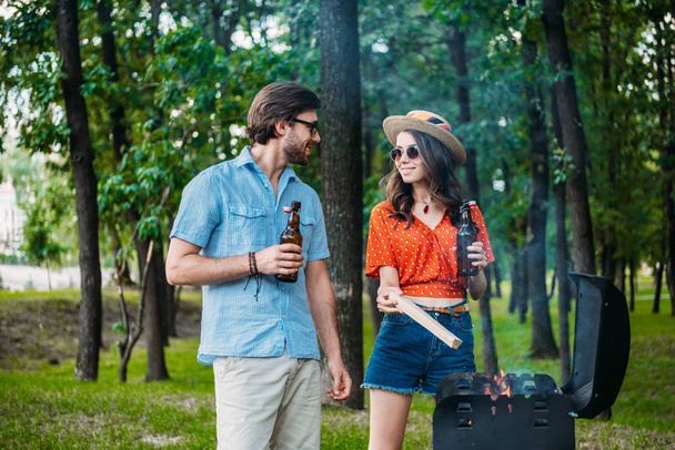 smiling couple in sunglasses with beer setting fire on grill together - Foto, Imagem