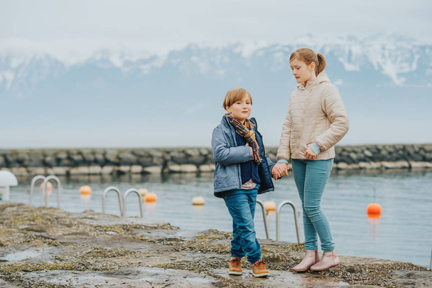 Retrato al aire libre de dos adorables niños jugando juntos al lado del lago en un día frío, usando chaquetas cálidas de invierno.
 - Foto, imagen