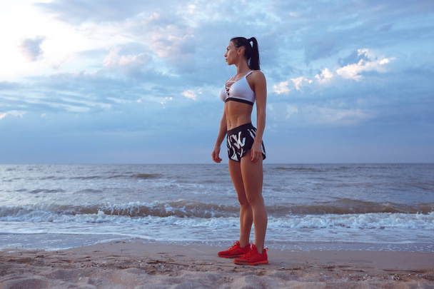 Девушка делает разминку перед занятиями спортом рано утром на берегу моря. Девушка спортивного телосложения с сухой мышечной массой
. - Фото, изображение