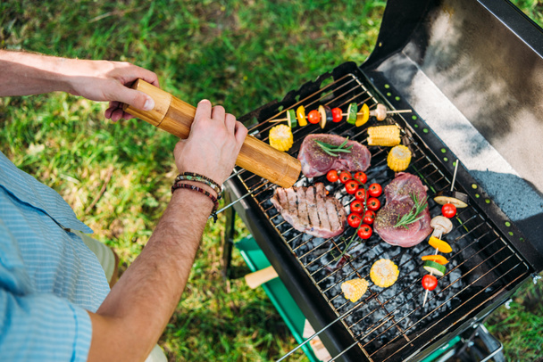 plan recadré de l'homme avec broyeur cuisson des aliments sur le gril pendant le barbecue dans le parc
 - Photo, image