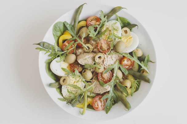 Nicoise-salaatti tonnikalasäilykkeiden, munien, vihreiden papujen, rucolan, paprikan, pinaatin, kirsikkatomaattien, kurkun ja oliivien kanssa valkoisella pöydällä. Tasapainoinen ateria
 - Valokuva, kuva
