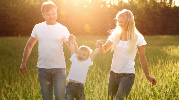 Mãe pai e filho caminham no campo com picos em camisetas brancas e jeans divertidos balançando nas mãos
 - Filmagem, Vídeo
