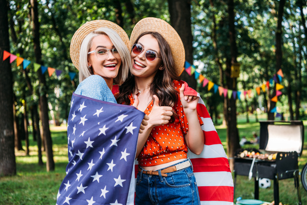 πορτρέτο του happy γυναίκες σε καπέλα και γυαλιά ηλίου με αμερικανική σημαία στο πάρκο - Φωτογραφία, εικόνα