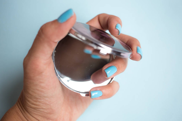women's hand with nail Polish holding a mirror on the light blue background - Fotoğraf, Görsel