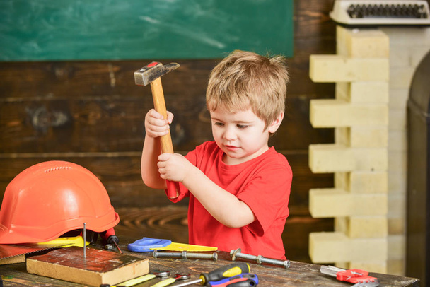 Toddler on busy face plays with hammer tool at home in workshop. Child cute and adorable playing as builder or repairer, repairing or handcrafting. Kid boy play as handyman. Handcrafting concept - Φωτογραφία, εικόνα