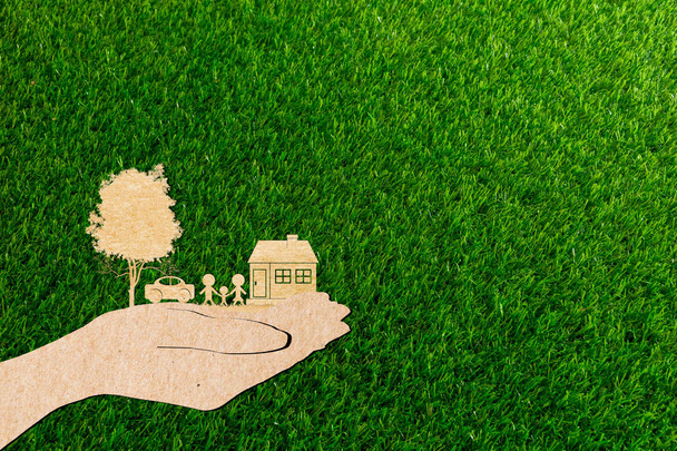 mãos segurando casa família carro e árvore de grama fundo papel corte
 - Foto, Imagem