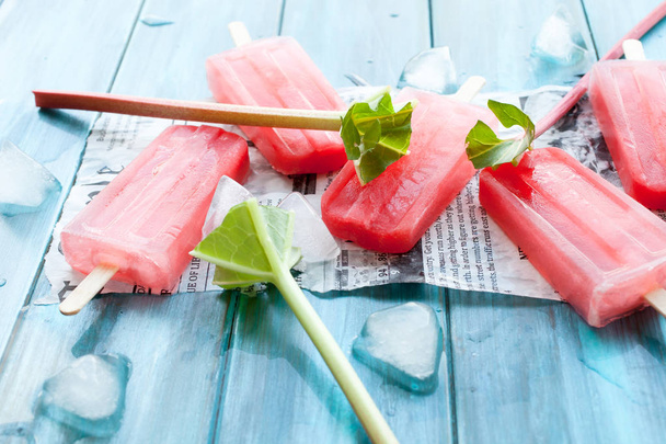 Refreshing rhubarb popsicles on blue wooden background with newspaper article - Fotografie, Obrázek