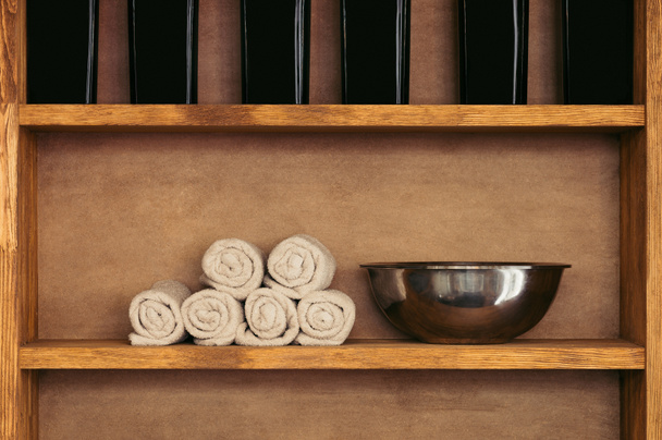 close-up view of empty metal bowl, rolled towels and glass containers on wooden shelves  - Photo, Image