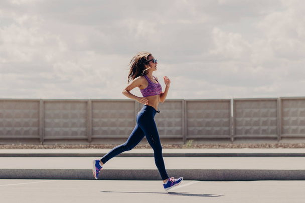 People and workout concept. Motivated female with healthy slim body, covers long distance running, likes sport and outdoor physical activities, has cardio training. Woman runner in open air. - Photo, Image