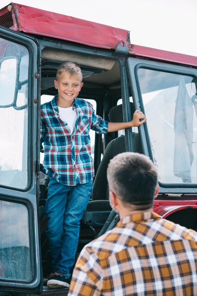 вид ззаду батька, дивлячись на щасливого сина, що стоїть у тракторі
 - Фото, зображення