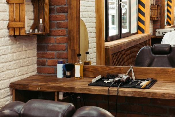 профессиональные инструменты парикмахера на деревянной полке возле зеркала в современной парикмахерской
 - Фото, изображение