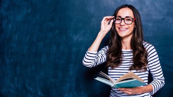 Young woman posing with book on chalkboard background - 写真・画像