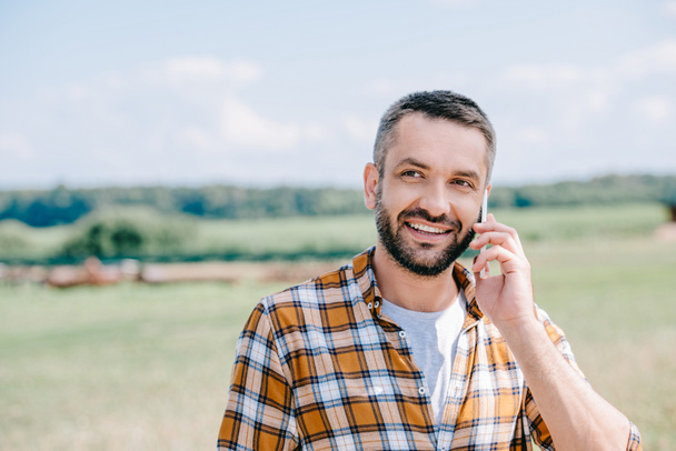 smiling middle aged farmer talking by smartphone in field - Photo, Image