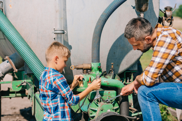 батько і син ремонтують сільськогосподарську машину разом
 - Фото, зображення