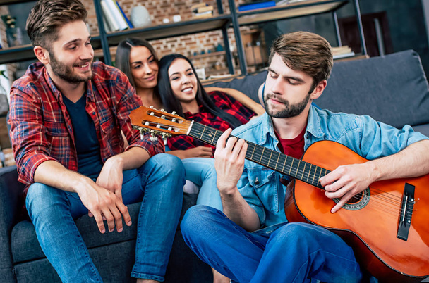 Group of young friends relaxing at home and man playing guitar - Foto, Imagem