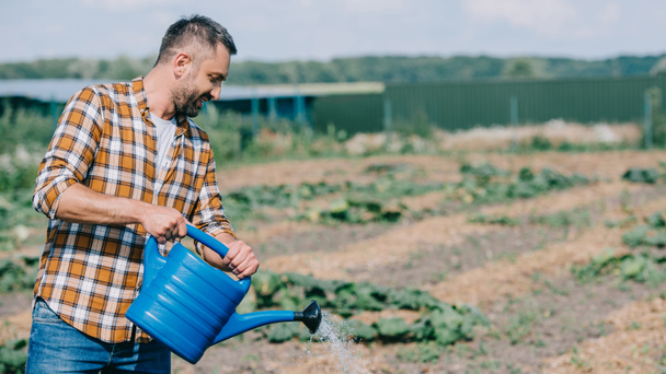 farmer in checkered shirt holding watering can and working in field  - Foto, Imagem