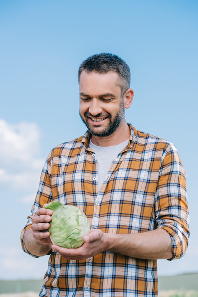 happy handsome farmer holding fresh cabbage outdoors - Foto, immagini