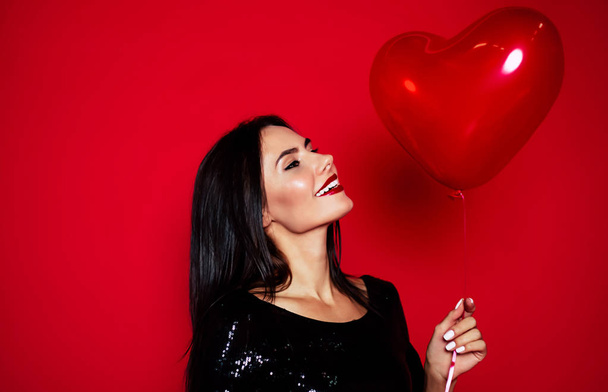 Young brunette woman with red balloon posing on red background - Foto, Imagen