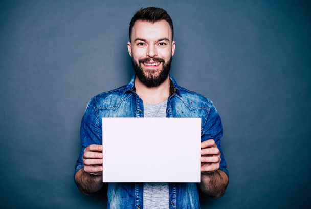 Beard man holding blank sheet of paper over grey background - Фото, зображення