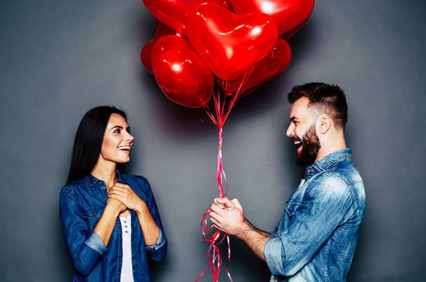 Young caucasian couple posing with red air balloons on grey background - Fotoğraf, Görsel