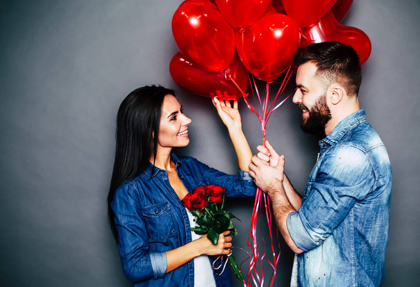 Young caucasian couple posing with red air balloons on grey background - Fotoğraf, Görsel