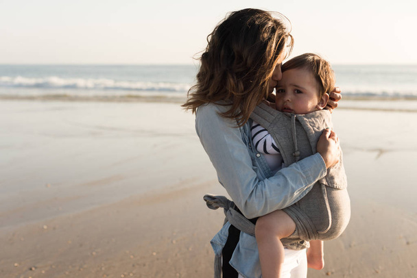 Madre con ergobaby llevando a un niño pequeño en la playa
 - Foto, imagen