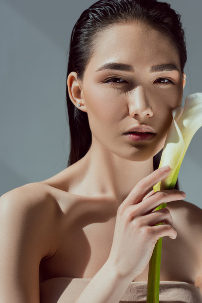attractive naked asian woman with calla flower, isolated on grey - Photo, Image