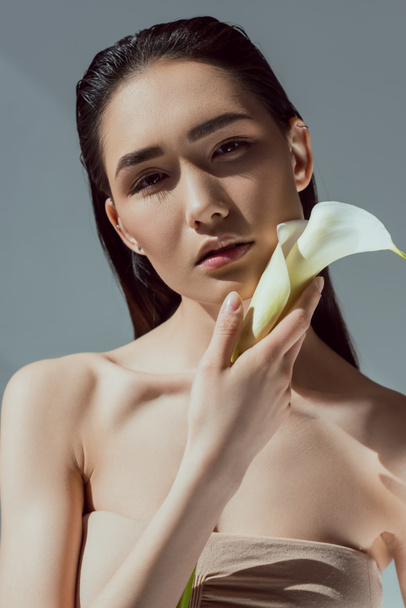 tender asian young woman with calla flower, isolated on grey - Zdjęcie, obraz