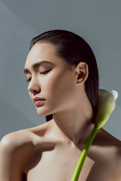 tender asian girl with closed eyes holding calla flower, isolated on grey - Fotó, kép