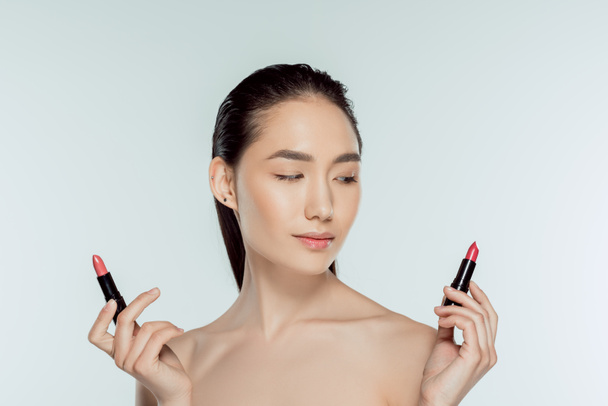 beautiful asian woman choosing red lipsticks, isolated on grey - Fotografie, Obrázek