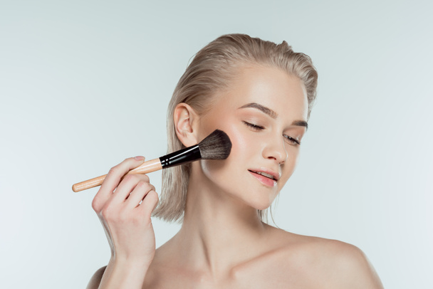 beautiful woman applying powder with cosmetic brush, isolated on grey - Fotó, kép