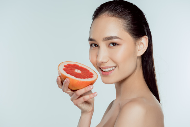 glimlachend Aziatisch meisje houdt van grapefruit, geïsoleerd op grijs - Foto, afbeelding