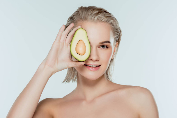smiling blonde girl posing with avocado, isolated on grey - Zdjęcie, obraz